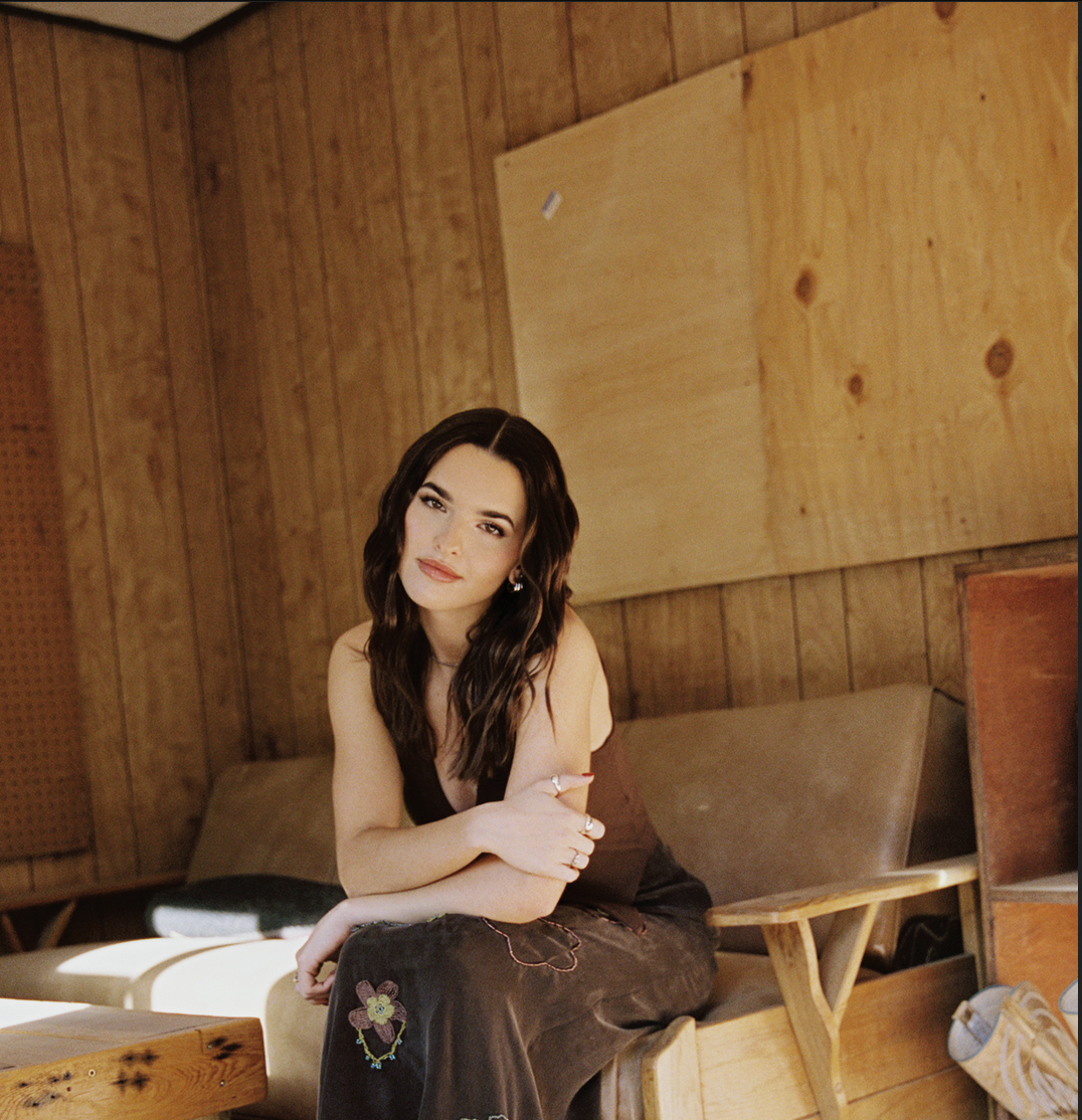 A woman with brunette hair is sitting on a couch, and her arms crossed.